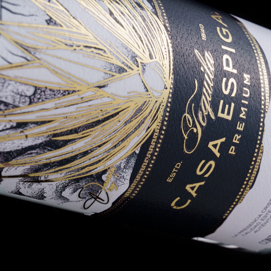 Close-up of a premium home wine bottle label by Casa Espiga, featuring a black textured band with gold lettering and a large gold feather graphic on a white background.